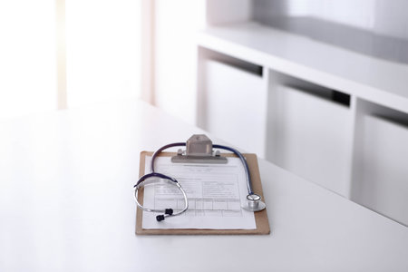 Stethoscope and clipboard with medication history records are on the table at sunny doctors working place. Medicine conceptの写真素材