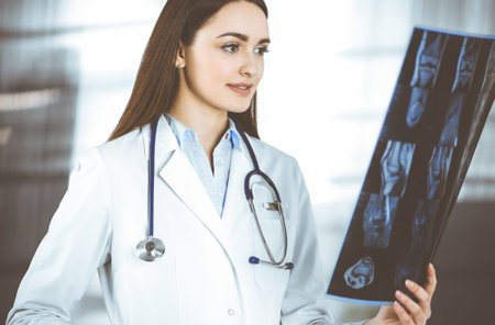 Professional young woman-doctor is looking at her patients roentgenogram. Physician at work in a...