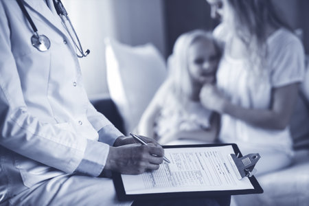 Doctor and patient. Pediatrician using clipboard while examining little girl with her mother at home. Sick and unhappy child at medical exam. Medicine conceptの写真素材