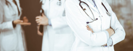 Unknown young woman doctor is standing with arms crossed in clinic.
