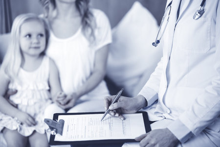 Doctor and patient. Pediatrician using clipboard while examining little girl with her mother at home. Happy cute caucasian child at medical exam. Medicine conceptの写真素材