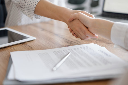 Business people shaking hands above contract papers just signed on the wooden table, close up....