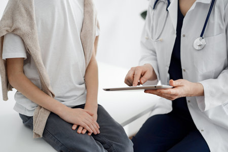 Doctor and child patient. The doctor is using tablet computer and is ready to examine the boy. The concept of ideal health in medicineの写真素材