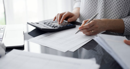 Woman accountant using a calculator and laptop computer while counting taxes for a client. Business audit and finance conceptsの写真素材