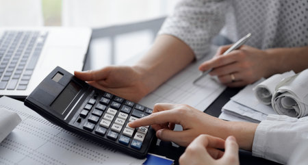 Woman accountant using a calculator and laptop computer while counting taxes for a client. Business audit and finance conceptsの写真素材