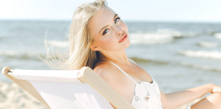 Happy blonde woman relaxing on a wooden deck chair at the ocean beachの写真素材