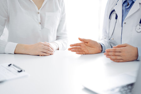 Doctor and patient discussing current health questions while sitting near of each other at the table in clinic, just hands closeup. Medicine conceptの写真素材