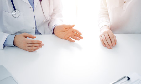 Doctor and patient discussing current health questions while sitting near of each other at the table in clinic, just hands closeup. Medicine conceptの写真素材