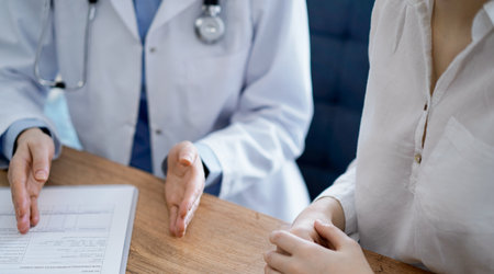 Doctor and patient discussing something while sitting near each other at the wooden desk in clinic, view from above. Medicine conceptの写真素材