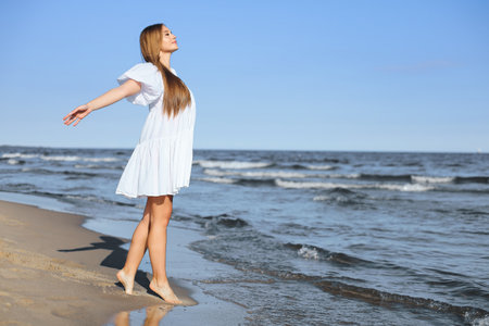 Happy smiling beautiful woman is walking on the ocean beach with open armsの写真素材