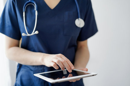 Doctor woman using tablet computer while standing near panorama window in clinic, close up. Physician or surgeon at work. Medicine conceptの写真素材