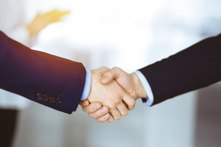 Business people shaking hands at meeting or negotiation, close-up. Group of unknown businessmen and a woman standing in a sunny modern office. Teamwork, partnership and handshake conceptの写真素材