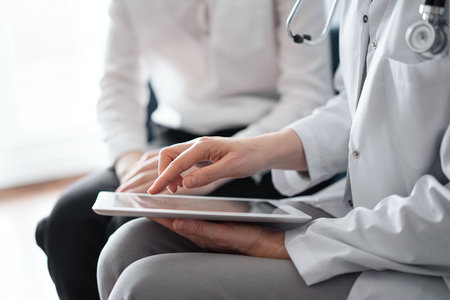 Doctor and patient sitting at sofa in clinic office. The focus is on female physicians hands using tablet computer, close up. Perfect medical service and medicine conceptの写真素材