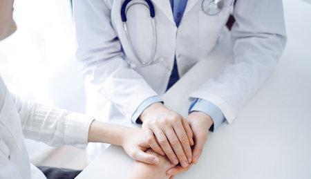 Doctor and patient sitting near each other at the table in clinic office. The focus is on female physicians hands reassuring woman, only hands, close up. Medicine conceptの写真素材