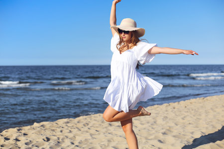 Happy blonde woman having fun on the ocean beach in a white dress and sunglassesの写真素材