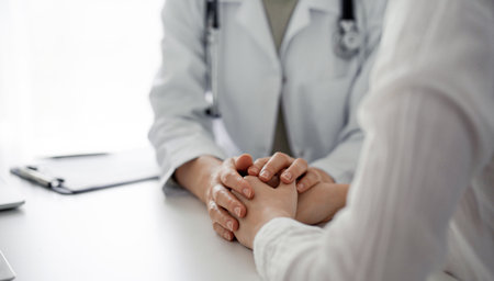 Doctor and patient sitting at the desk in clinic office. The focus is on female physicians hands reassuring woman, close up. Perfect medical service, empathy, and medicine conceptの写真素材