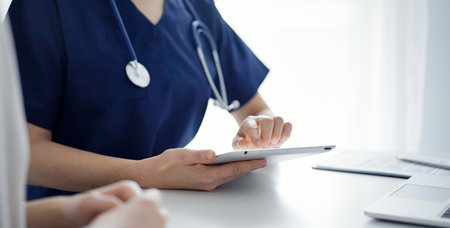 Doctor and patient talking to each other in clinic while sitting and using tablet computer, close up. Medicine conceptの写真素材