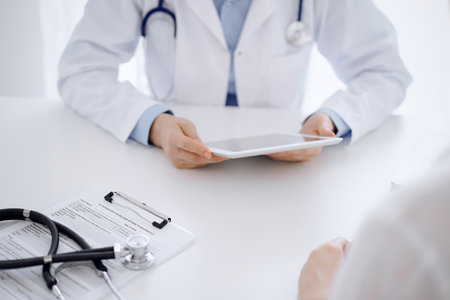 Stethoscope lying on the tablet computer in front of a doctor and patient sitting opposite each other and using tablet computer at the background . Medicine, healthcare conceptの写真素材