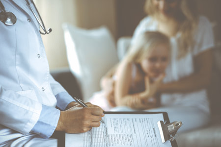 Doctor and patient. Pediatrician using clipboard while examining little girl with her mother at home. Happy cute caucasian child at medical exam. Medicine conceptの写真素材