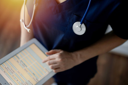 Doctor woman using tablet computer while standing near panorama window in clinic, close up. Physician or surgeon at work. Medicine conceptの写真素材