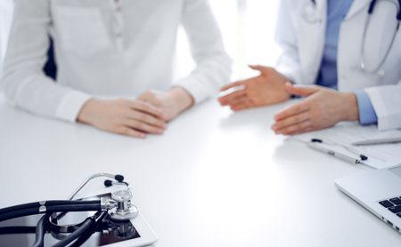 Stethoscope lying on the tablet computer in front of a doctor and patient sitting near of each other at the background. Medicine, healthcare conceptの写真素材