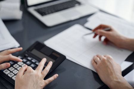 Woman accountant using a calculator and laptop computer while counting taxes for a client. Business audit and finance conceptsの写真素材