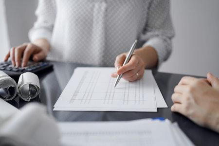 Woman accountant using a calculator and laptop computer while counting taxes for a client. Business...