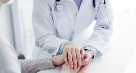 Doctor and patient sitting at the table in clinic office. The focus is on female physicians hands reassuring woman, only hands close up. Medicine conceptの写真素材