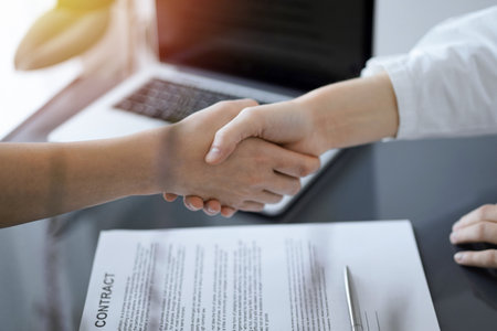 Business people shaking hands above contract papers just signed on the white table, closeup. Lawyers at meeting. Teamwork, partnership, success conceptの写真素材