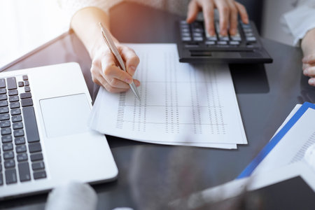 Woman accountant using a calculator and laptop computer while counting taxes for a client. Business audit conceptsの写真素材