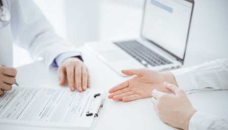 Doctor and patient discussing current health examination while sitting opposite each other at the desk in clinic. The focus is on female hands, close up. Medicine conceptの写真素材