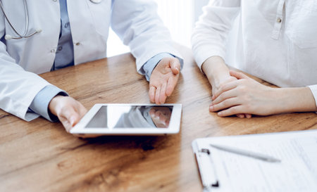 Doctor and patient sitting at the wooden desk in clinic. Female physicians hands pointing into...