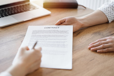 Business people signing contract papers while sitting at the wooden table in office, closeup. Partners or lawyers working together at meeting. Teamwork, partnership, success conceptの写真素材