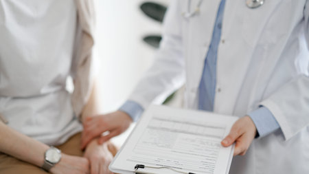 Doctor and patient in clinic. Friendly physician examining a young woman with a one hand while keeping a clipboard with medical records in another. Medicine conceptの写真素材