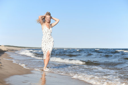 Happy blonde beautiful woman having fun on ocean beach while dancing in wavesの写真素材