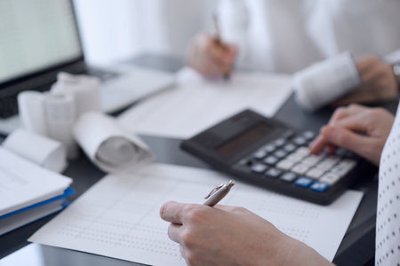 Two accountants use a calculator and laptop computer for counting taxes or revenue balance. Business, audit, and taxes conceptsの写真素材