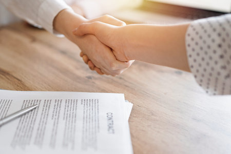 Business people shaking hands above contract papers just signed on the wooden table, close up....