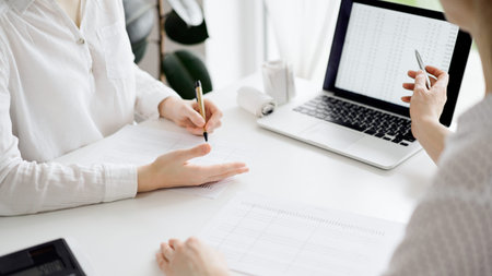 Two accountants using a laptop computer for counting taxes at white desk in office. Business Woman...