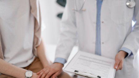 Doctor and patient discussing health exam results. Friendly physician reassuring a young woman by one hand while keeping clipboard with medical papers in another. Medicine conceptの写真素材