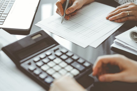 Woman accountant using a calculator and laptop computer while counting taxes for a client. Business audit and finance conceptsの写真素材