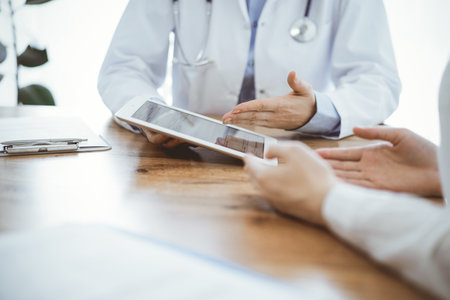 Doctor and patient sitting at the wooden desk in clinic. Female physicians hands pointing into laptop computer monitor, close up. Medicine conceptの写真素材