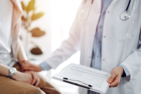 Doctor and patient discussing health exam results. Friendly physician reassuring a young woman by one hand while keeping clipboard with medical papers in another. Medicine conceptの写真素材