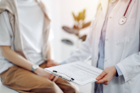 Doctor and patient discussing health exam results. Friendly physician reassuring a young woman by one hand while keeping clipboard with medical papers in another. Medicine conceptの写真素材
