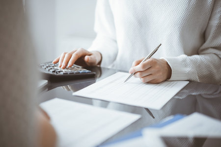 Woman accountant using a calculator and laptop computer while counting taxes for a client. Business...