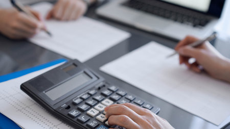 Two accountants use a calculator and laptop computer for counting taxes or revenue balance. Business, audit, and taxes conceptsの写真素材