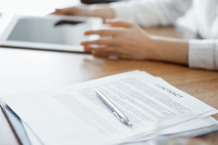 Contract papers are lying at the wooden desk while business people discussing something at the...