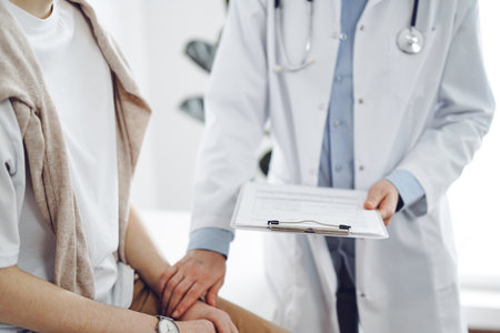 Doctor and patient in clinic. Friendly physician examining a young woman with a one hand while keeping a clipboard with medical records in another. Medicine conceptの写真素材