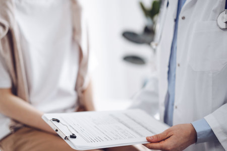 Doctor and patient discussing perfect health exam results. Friendly physician keeping with hands clipboard with medical papers near young woman. Medicine conceptの写真素材