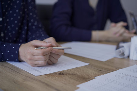 Accountants or auditors reviewing financial documents while sitting at the wooden desk in office. Professionals analyzing paper reports and using calculators, view above. Audit and taxes conceptの写真素材