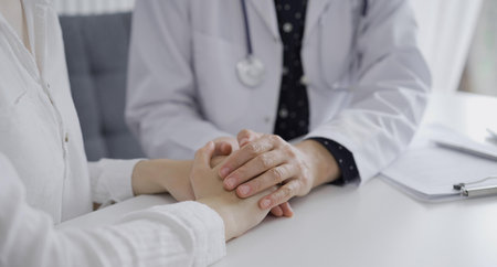 Doctor and a patient. The female physician, wearing a white medical coat over a dark blue dotted blouse, is reassuring a woman during a consultation in the clinic. Medicine conceptの写真素材